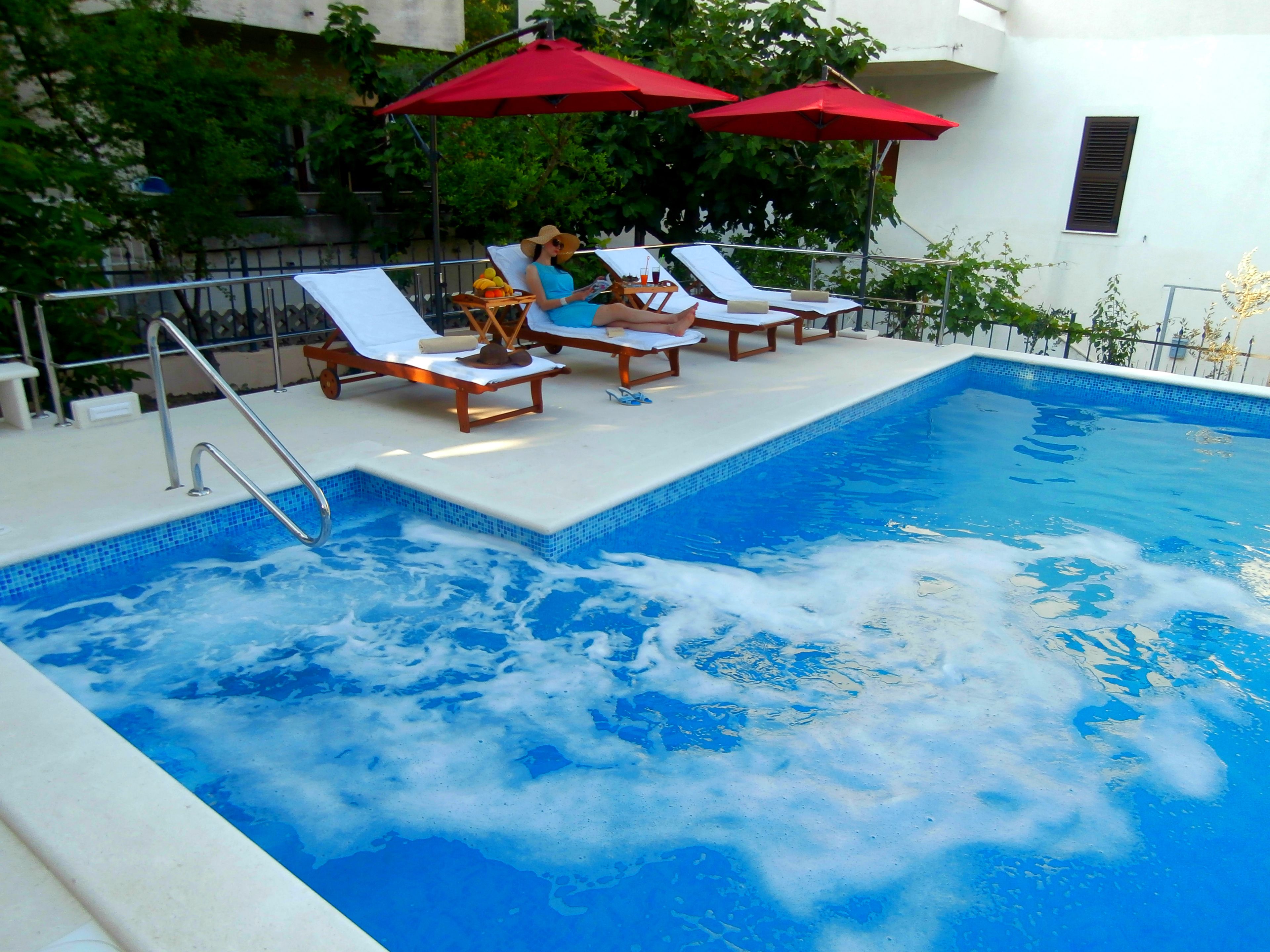 Una piscina con sillones de descanso y sombrillas rojas.