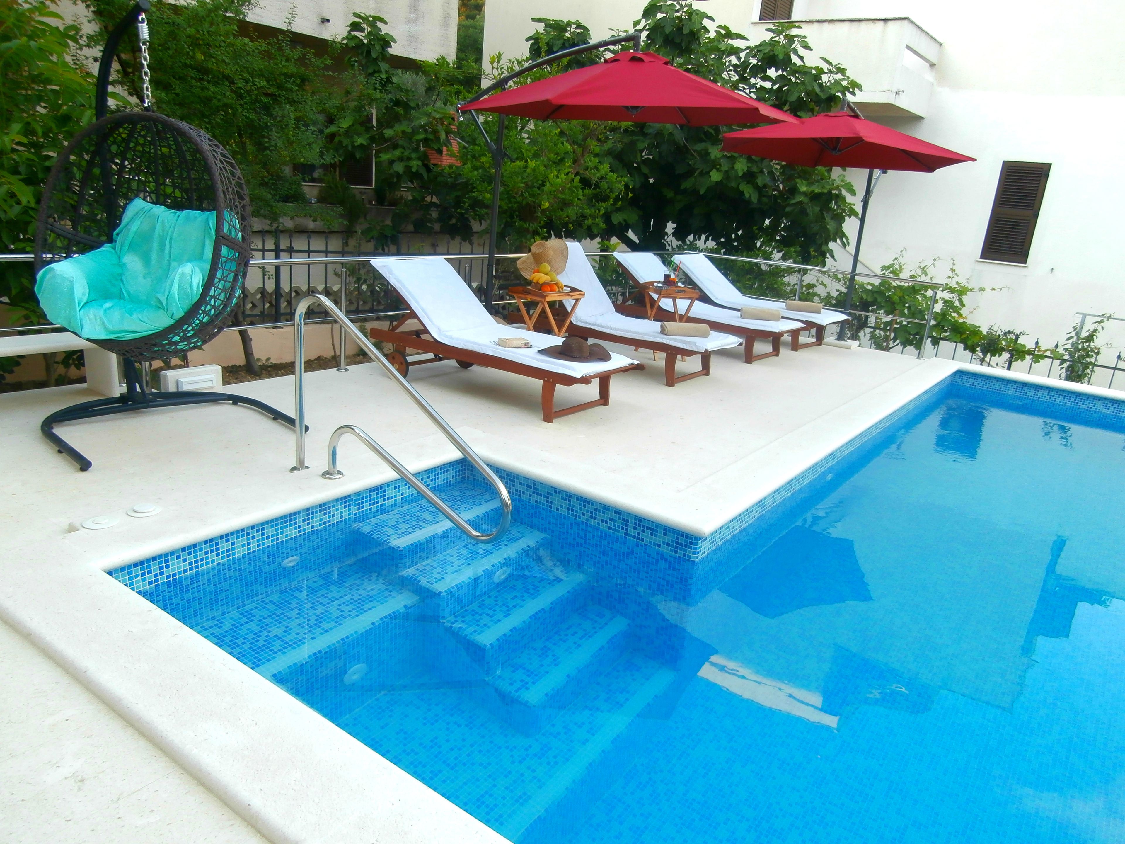 Ein Schwimmbecken mit einer Metallleiter, Liegestühlen und einer Hängematte.