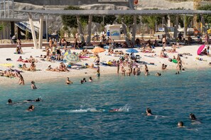 A crowded beach with people sunbathing, swimming, and playing in the water. - Apartments Cordis (Split)