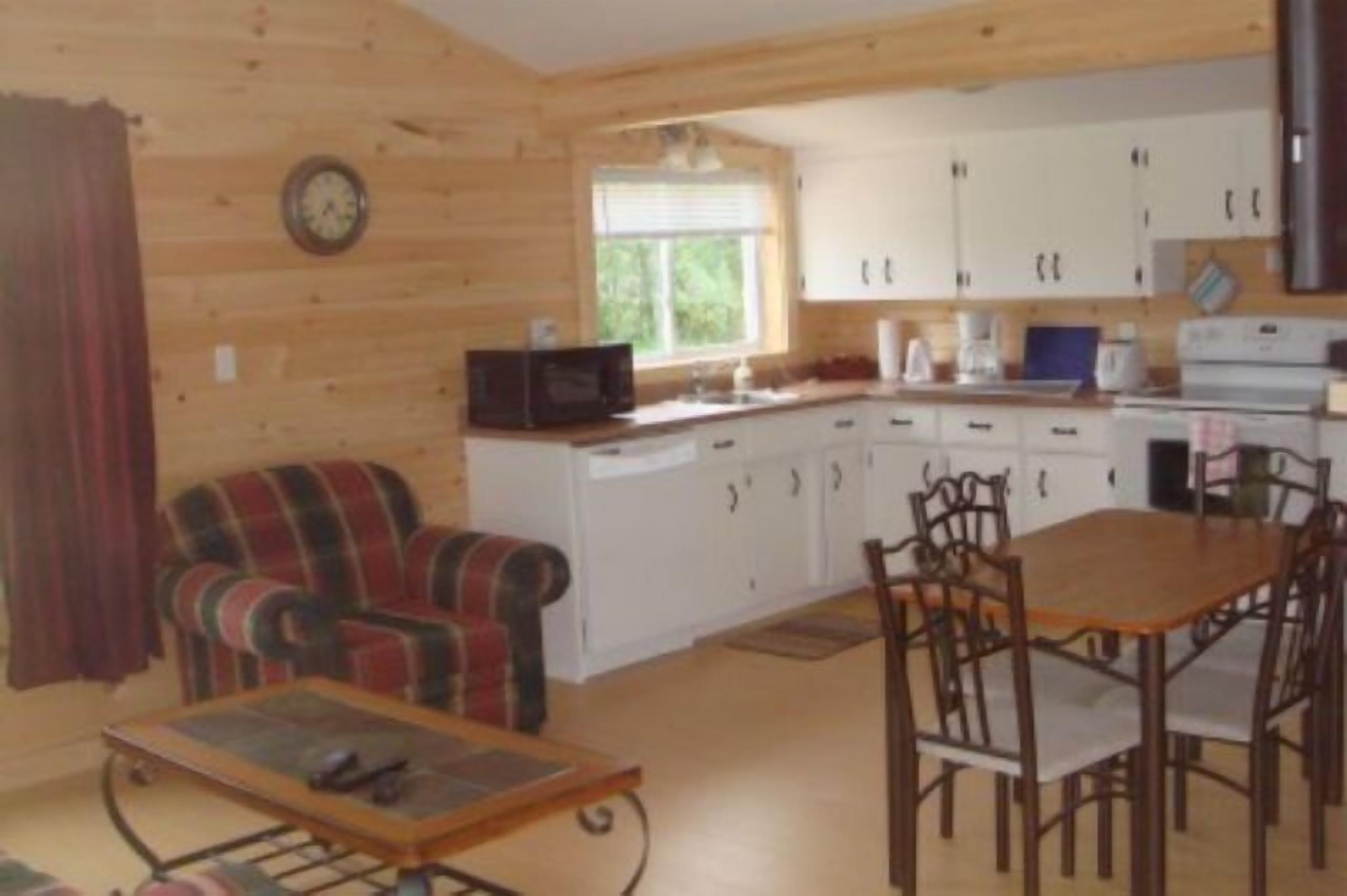 Una habitación acogedora de estilo cabaña con interior de madera, una mesa de comedor con sillas, un televisor y una zona de cocina con armarios y electrodomésticos.