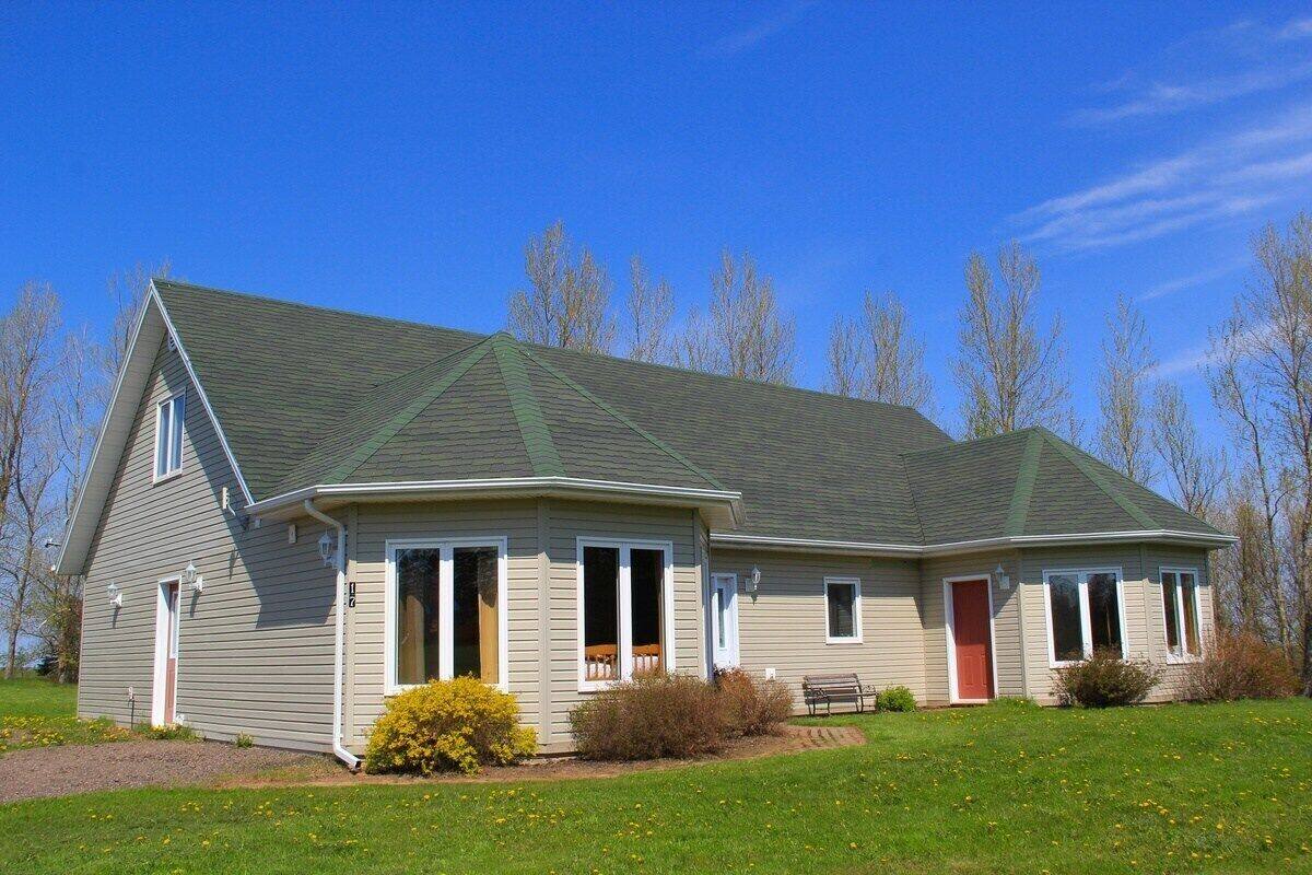 A two-story house with a green roof, a front porch, and a small front yard.