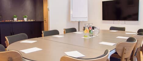 Un salón de conferencias con una mesa grande, sillas, una pizarra y un televisor de pantalla plana.