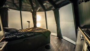 Habitación compacta con cama, un taburete pequeño y vistas al agua a través de amplios ventanales.