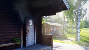 Una cabaña de madera con chimenea humeante, un banco de madera y una puerta con un letrero de número.