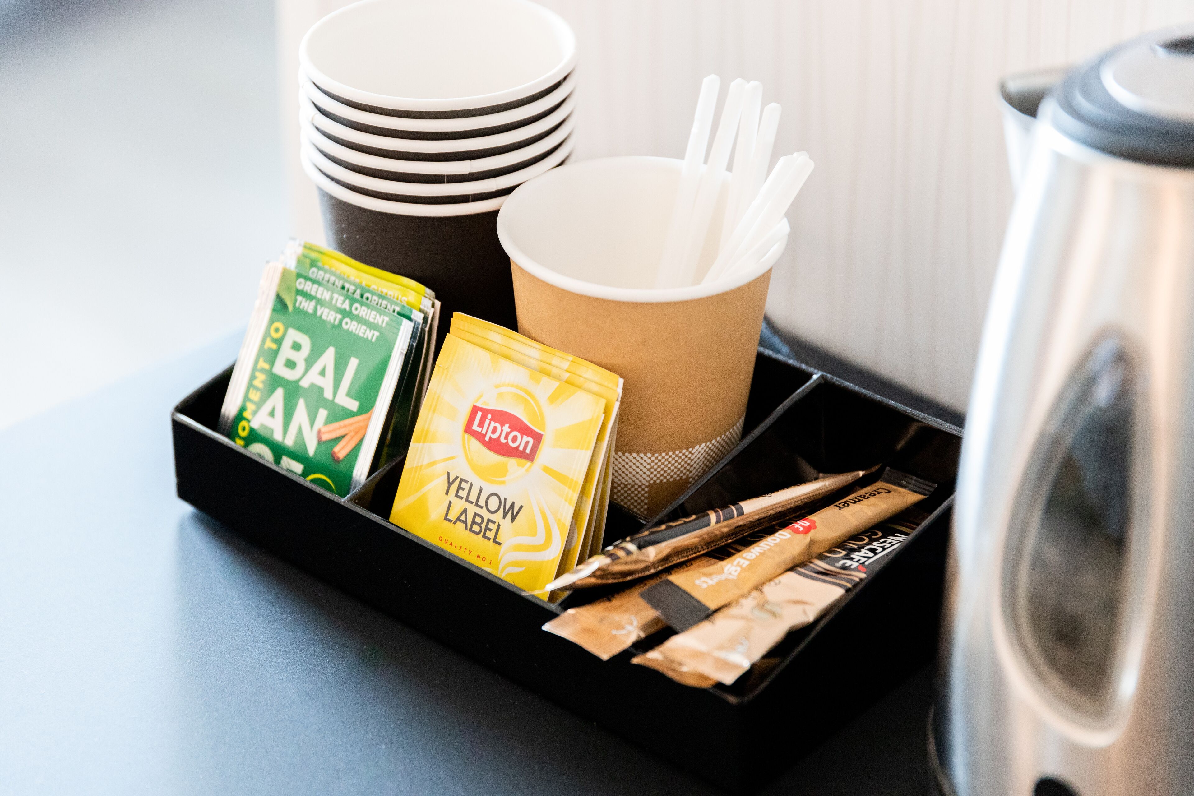 A tray with a coffee maker, paper cups, and Lipton tea bags.