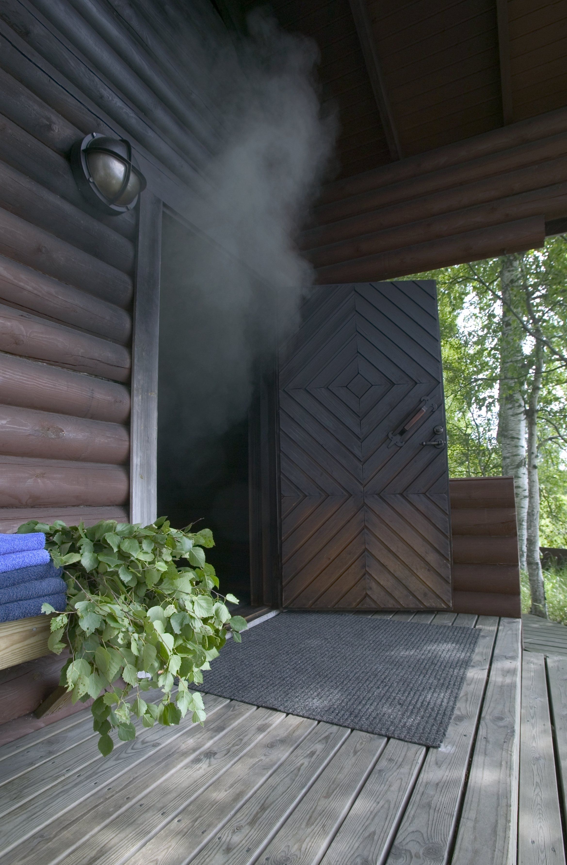 Una cabaña de madera con chimenea humeante, una puerta con diseño en chevron y una planta en maceta en el porche.