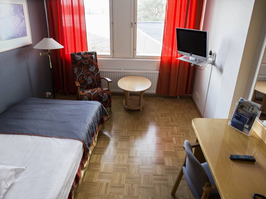 A hotel room with a bed, a desk, a chair, a TV, and a window with curtains.