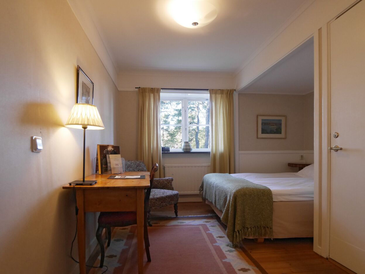 A bedroom with a bed, a desk with a chair, a window with curtains, and a door.