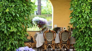 Un espace de restauration en plein air avec une table dressée pour quatre personnes, entouré de verdure et agrémenté d’une plante en pot aux fleurs bleues.