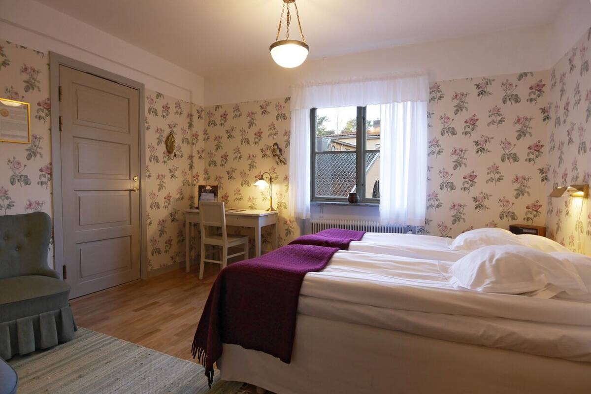 Een slaapkamer met twee bedden, een bureau, een stoel en een raam met uitzicht.