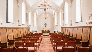 L’intérieur d’une église, avec des bancs en bois disposés en rangées, un autel central et un lustre.