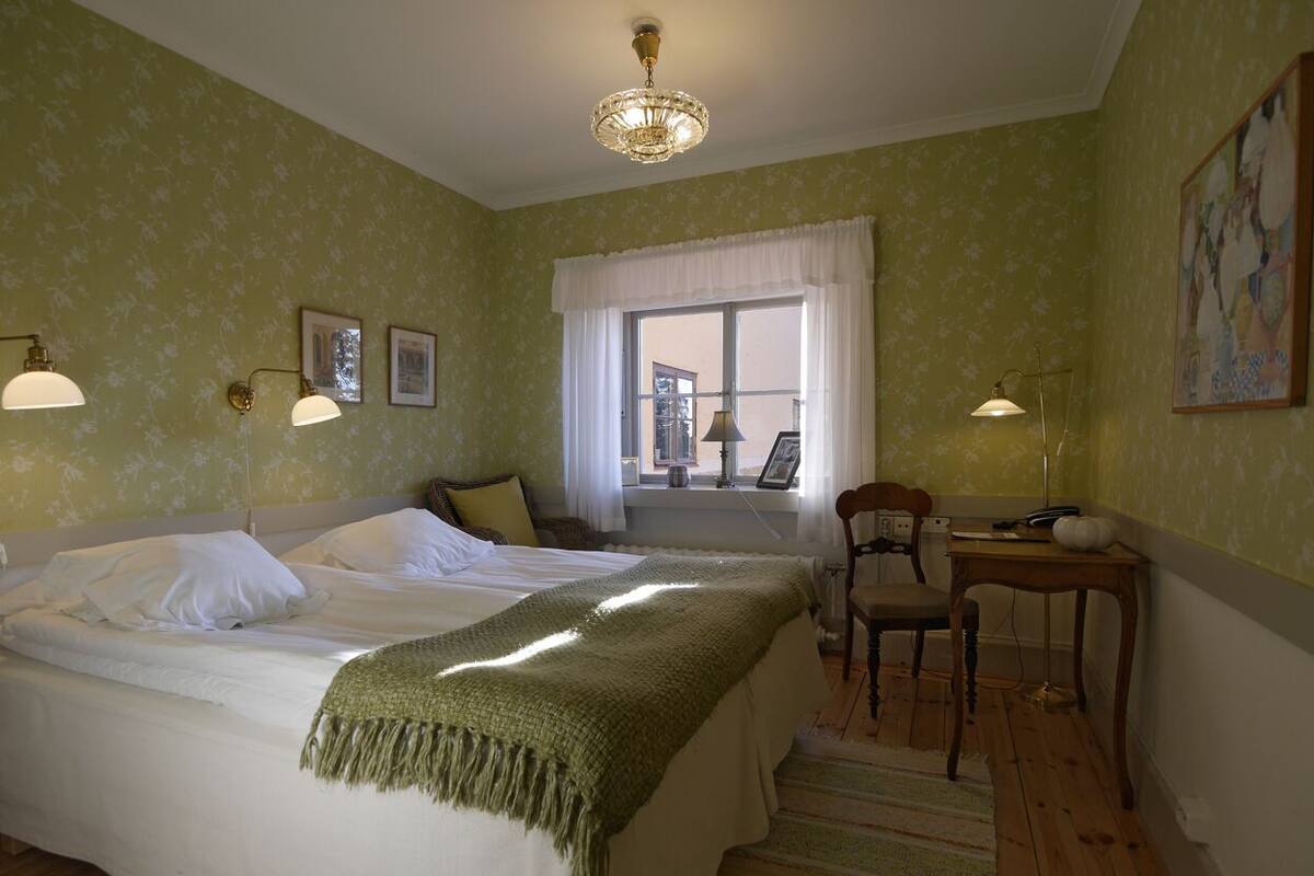 Een kamer met twee bedden, een bureau, een stoel, een raam met gordijnen en wandlampen.