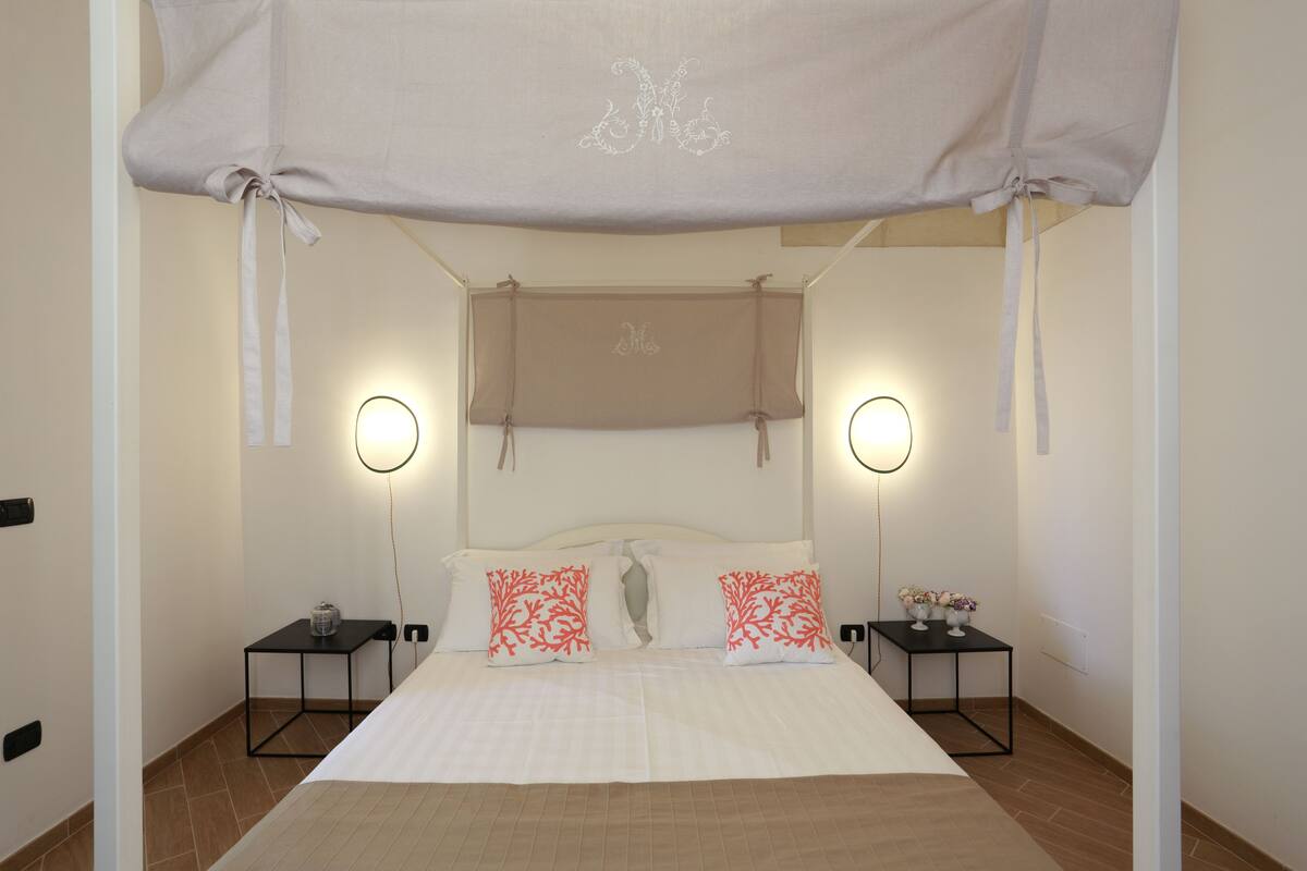 A bedroom with a canopy bed, two bedside tables with lamps, and a small table with flowers.