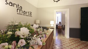 A reception area with a floral arrangement, a sign reading "Santa Marta Suites and apartments," and a hallway leading to another room.