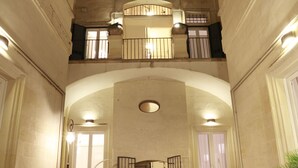 A courtyard with a dining area, tables, chairs, and a candle. There are potted plants and a wicker chair.