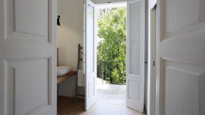 A bathroom with a white sink, a towel rack, and a door leading to a balcony with a view of trees.