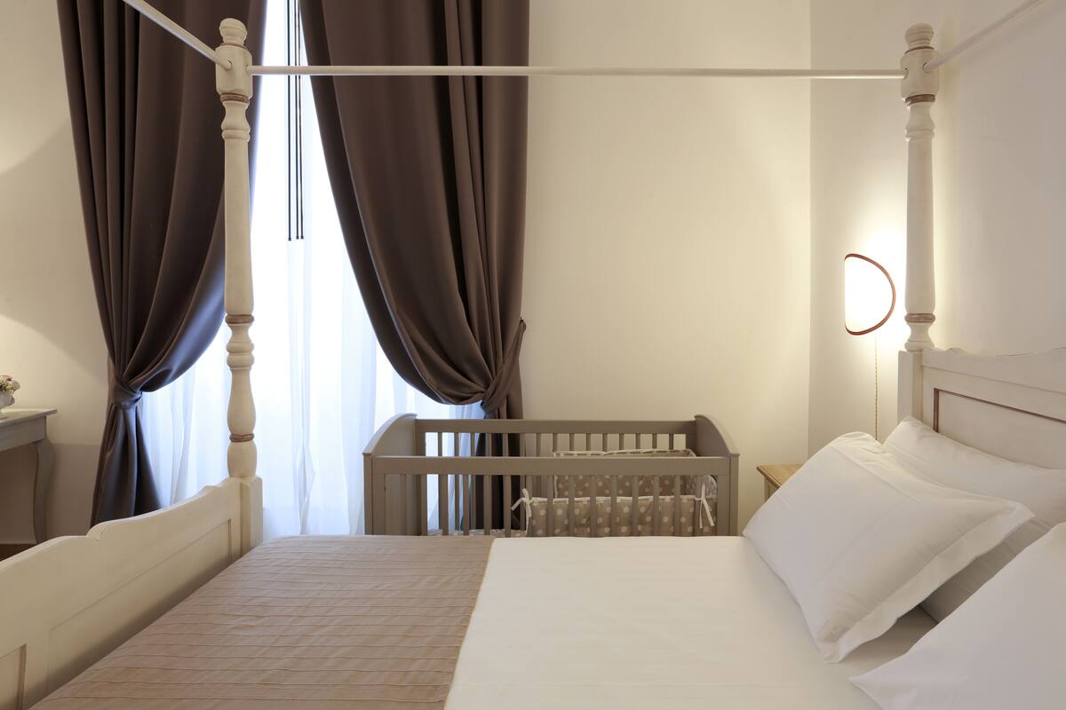 A bedroom with a four-poster bed, a crib, and a bedside table.