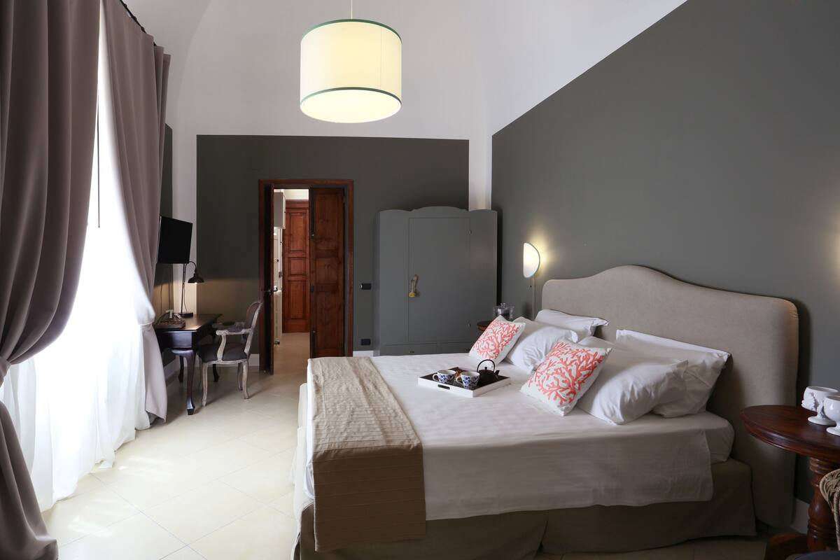 A hotel room with a bed, bedside table, lamp, and a desk with a chair.