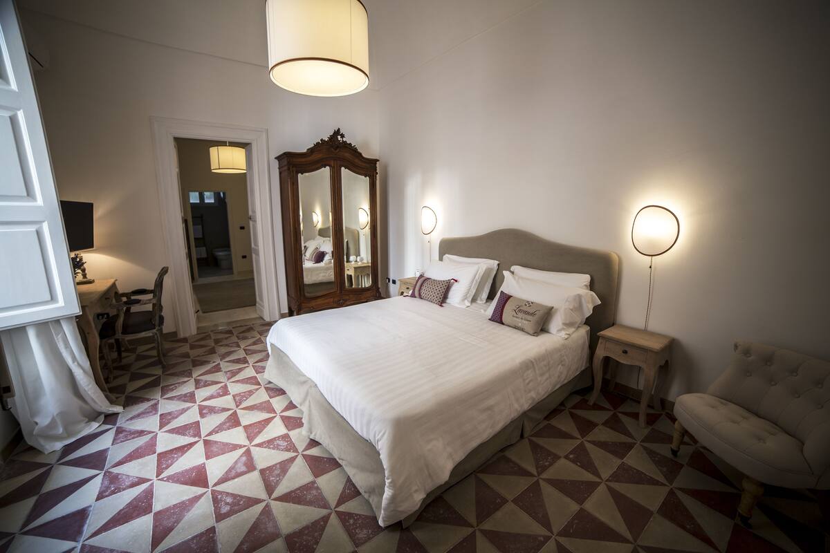A bedroom with a large bed, a dresser, a chair, and a mirror.