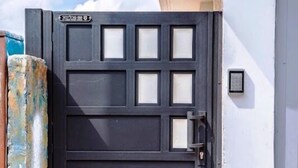 Ein schwarzes Metallgitter mit Zahlenschloss, ein kleiner Briefkasten und ein Betontritt führen zur Tür.