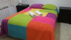 Ein Bett mit einer farbenfrohen Steude und zwei aufgerollten Handtüchern.