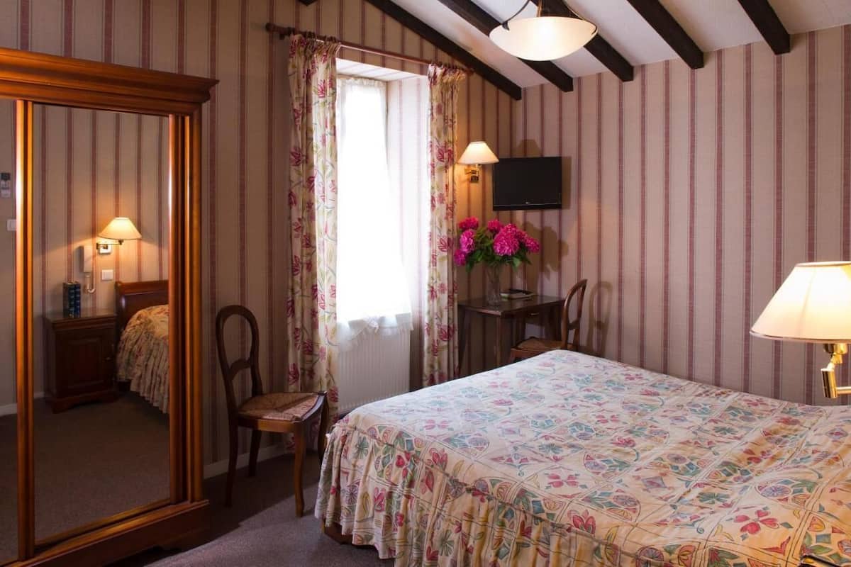A bedroom with a bed, a desk, a chair, a television, and a mirror.