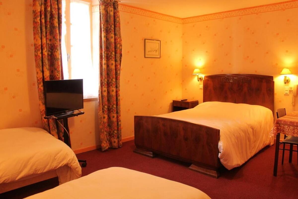 A hotel room with two beds, a television, a desk, and two wall-mounted lamps.