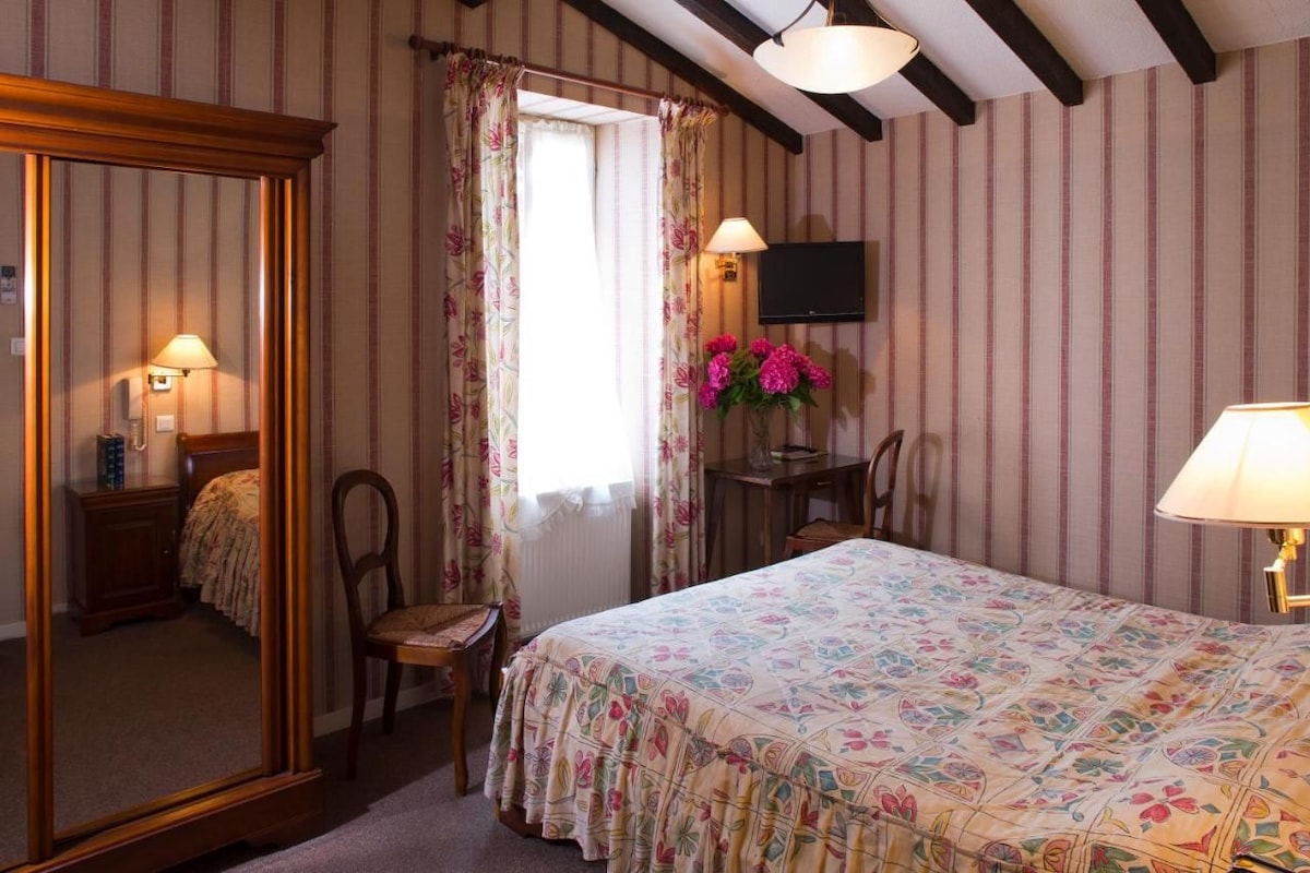 A bedroom with a bed, a desk, a chair, a television, and a mirror.