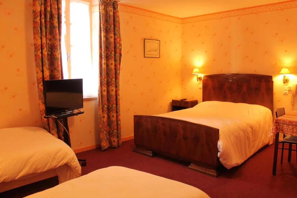 A hotel room with two beds, a television, a desk, and two wall-mounted lamps.