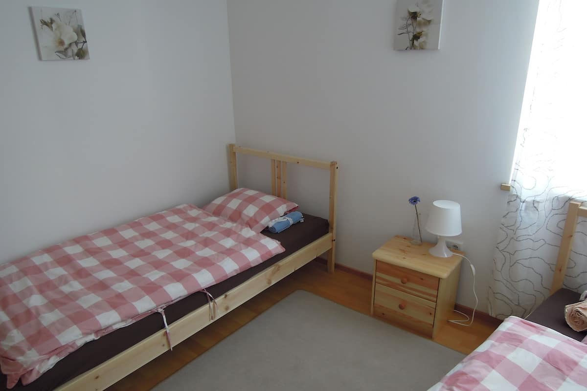 A single bed with a checkered bedspread, a bedside table with a lamp, and a small drawer.