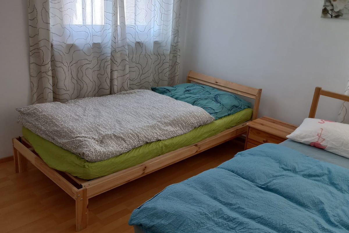 A single bed with a wooden frame, a green mattress, and a patterned blanket.