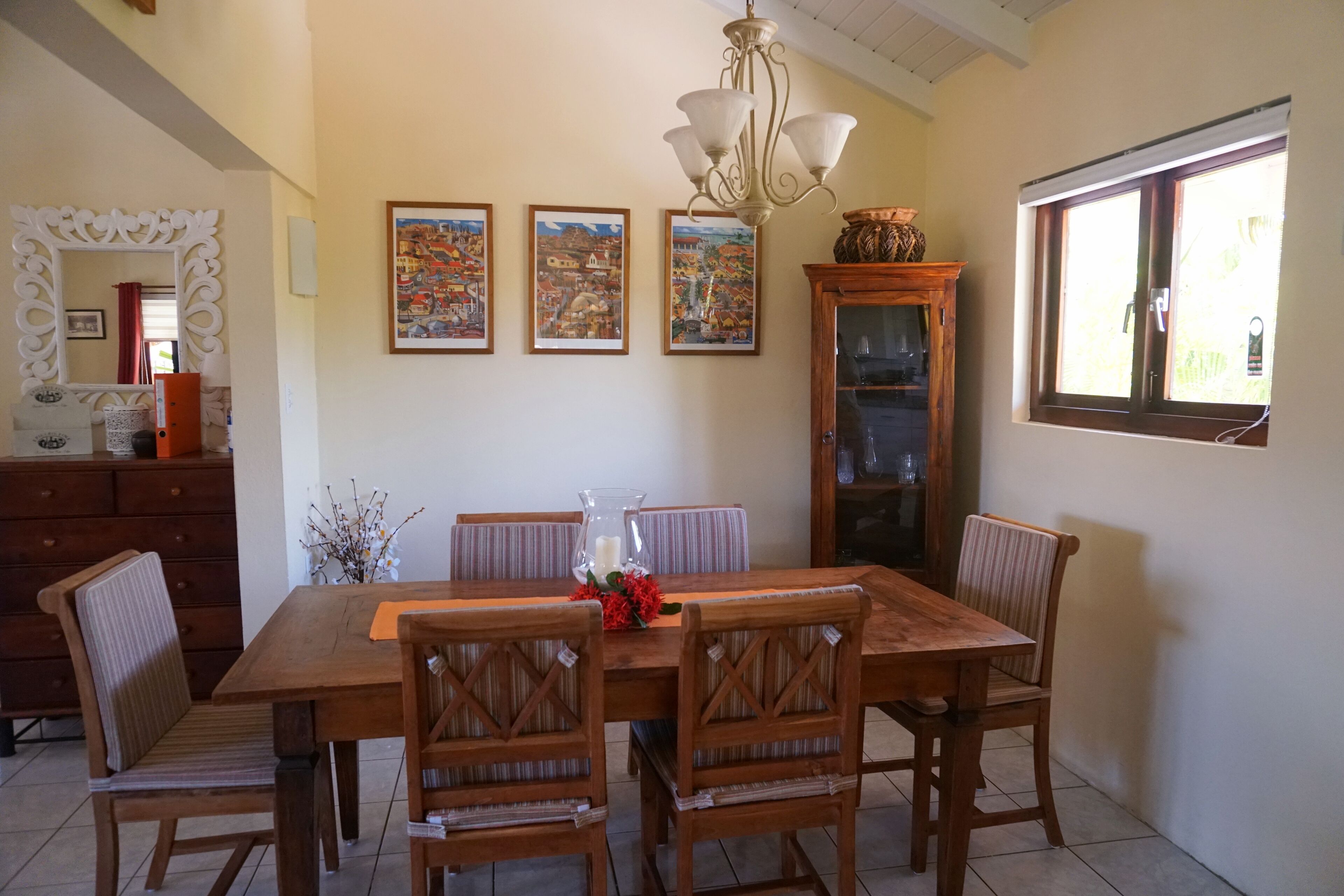 Un coin repas avec une table et des chaises en bois, un lustre et trois tableaux encadrés accrochés au mur.