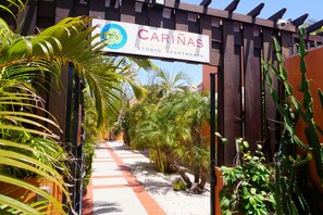 Un chemin menant à une entrée fermée par un portail, sur laquelle est apposée une enseigne indiquant « Carinas Studio Apartments ».