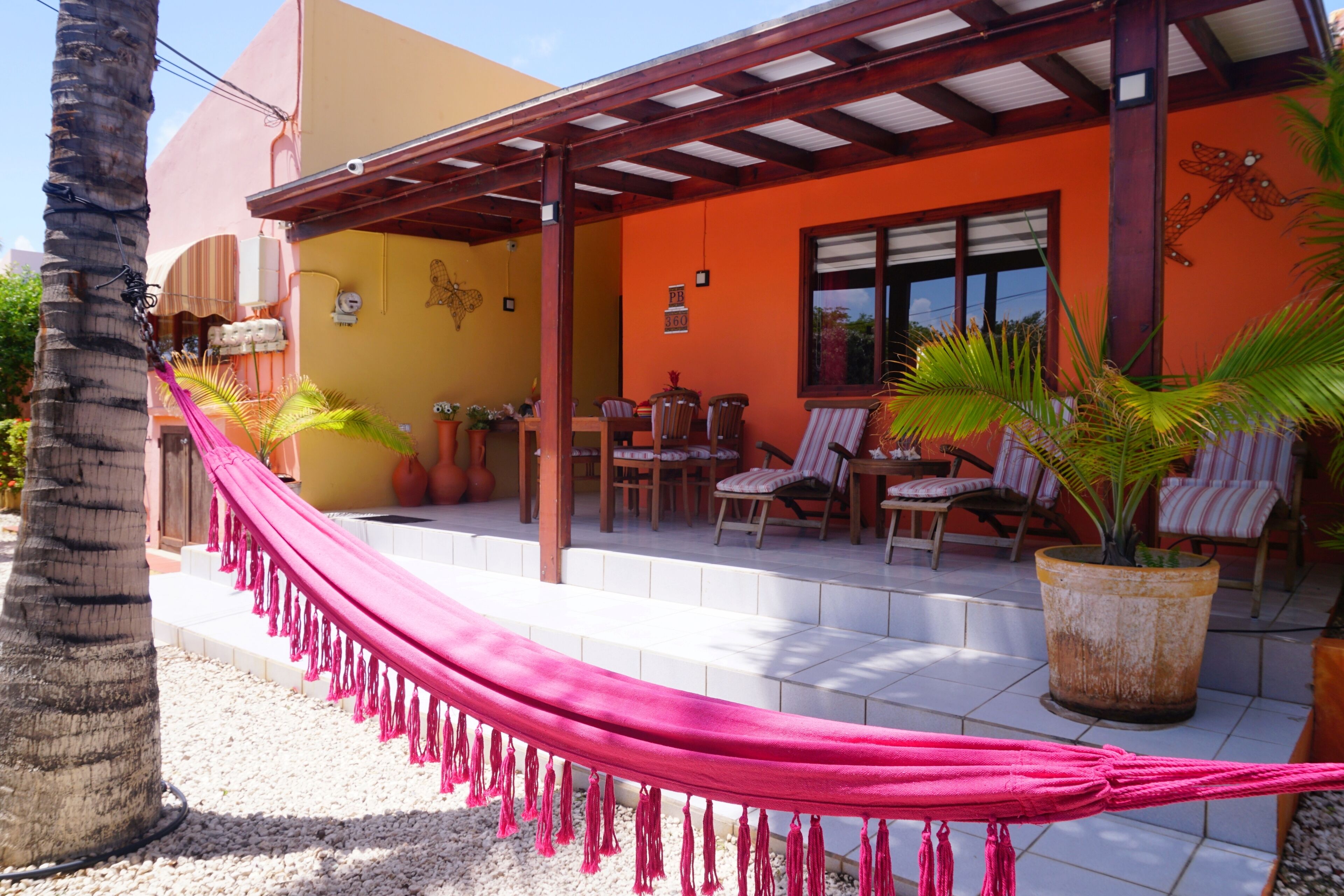 A covered patio with outdoor seating, a hammock, and potted plants.