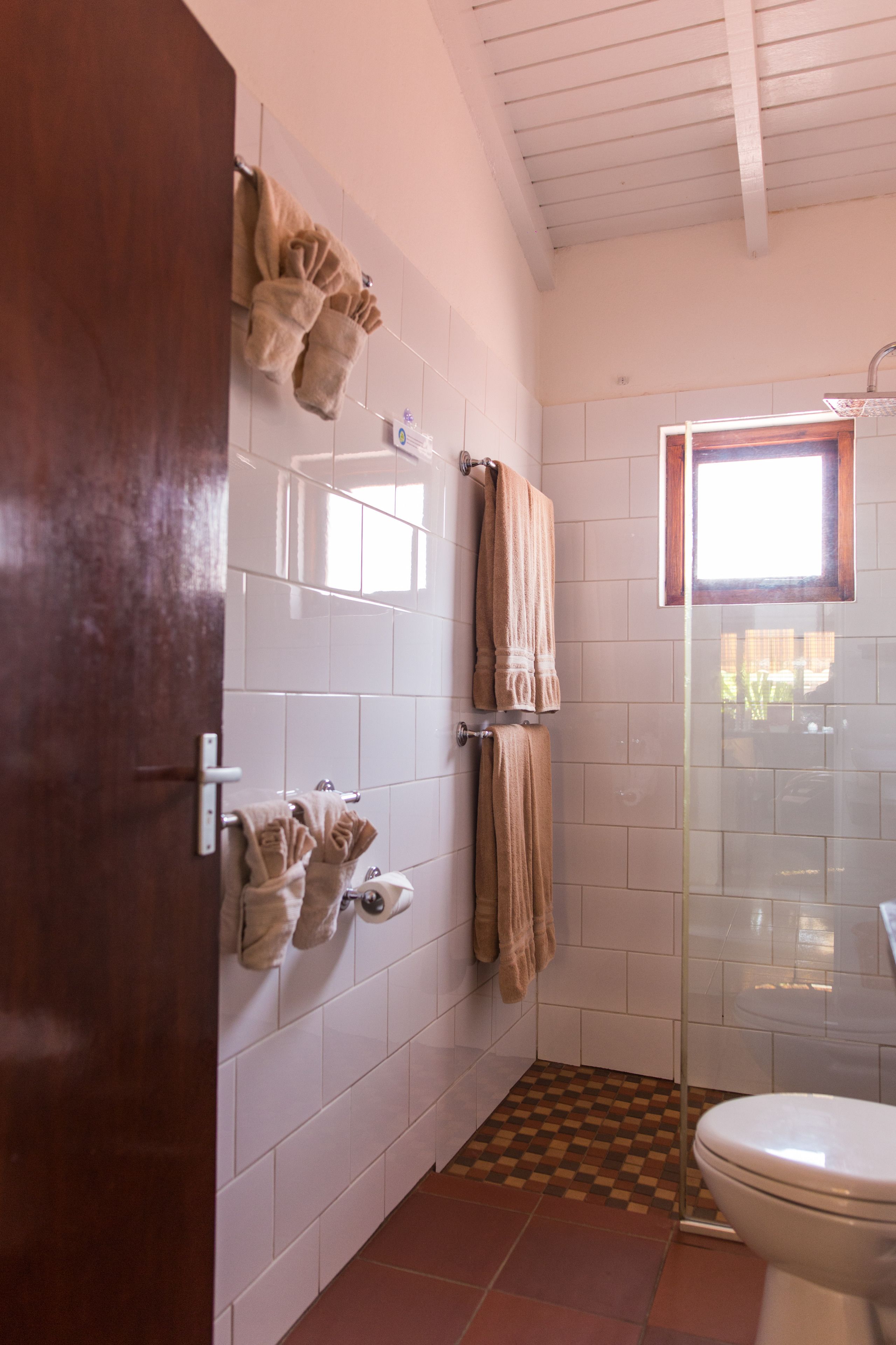 A bathroom with white tiled walls, a glass shower enclosure, and a brown checkered floor.
