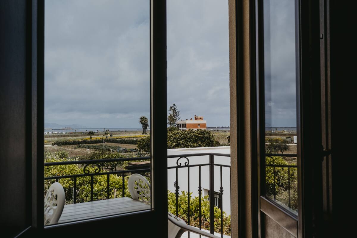 A balcony with a view of a coastal landscape, including a building and distant mountains.