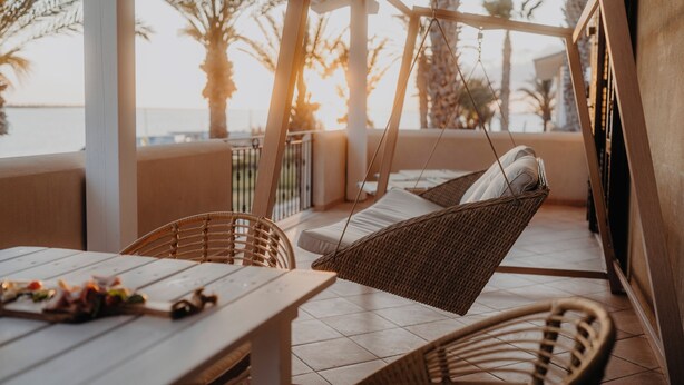 A sunlit outdoor seating area with wicker furniture and a view of palm trees. - Resort Santa Maria (Marsala)