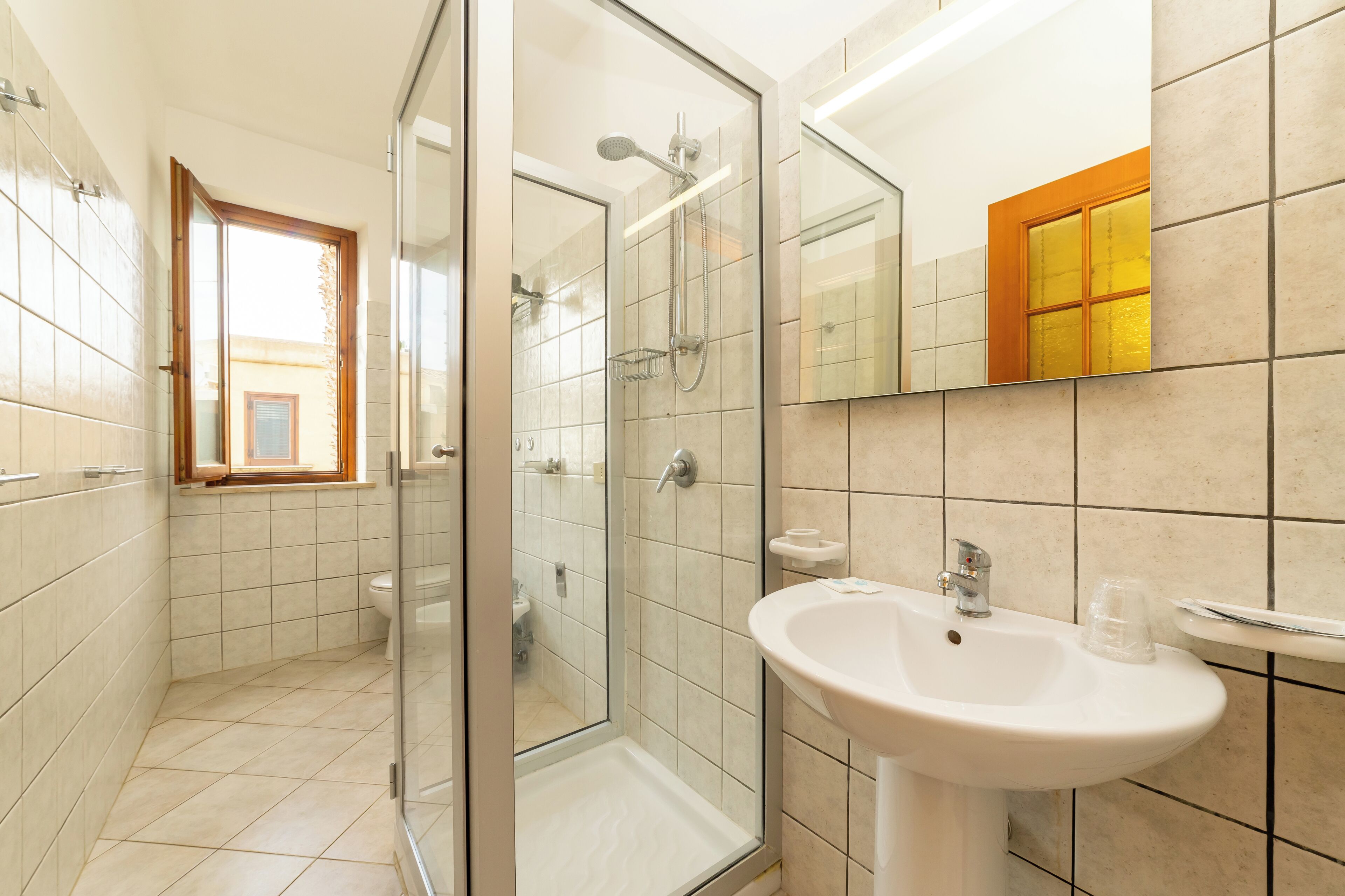 A modern bathroom with a glass shower enclosure, a white sink, and a window with a wooden frame.