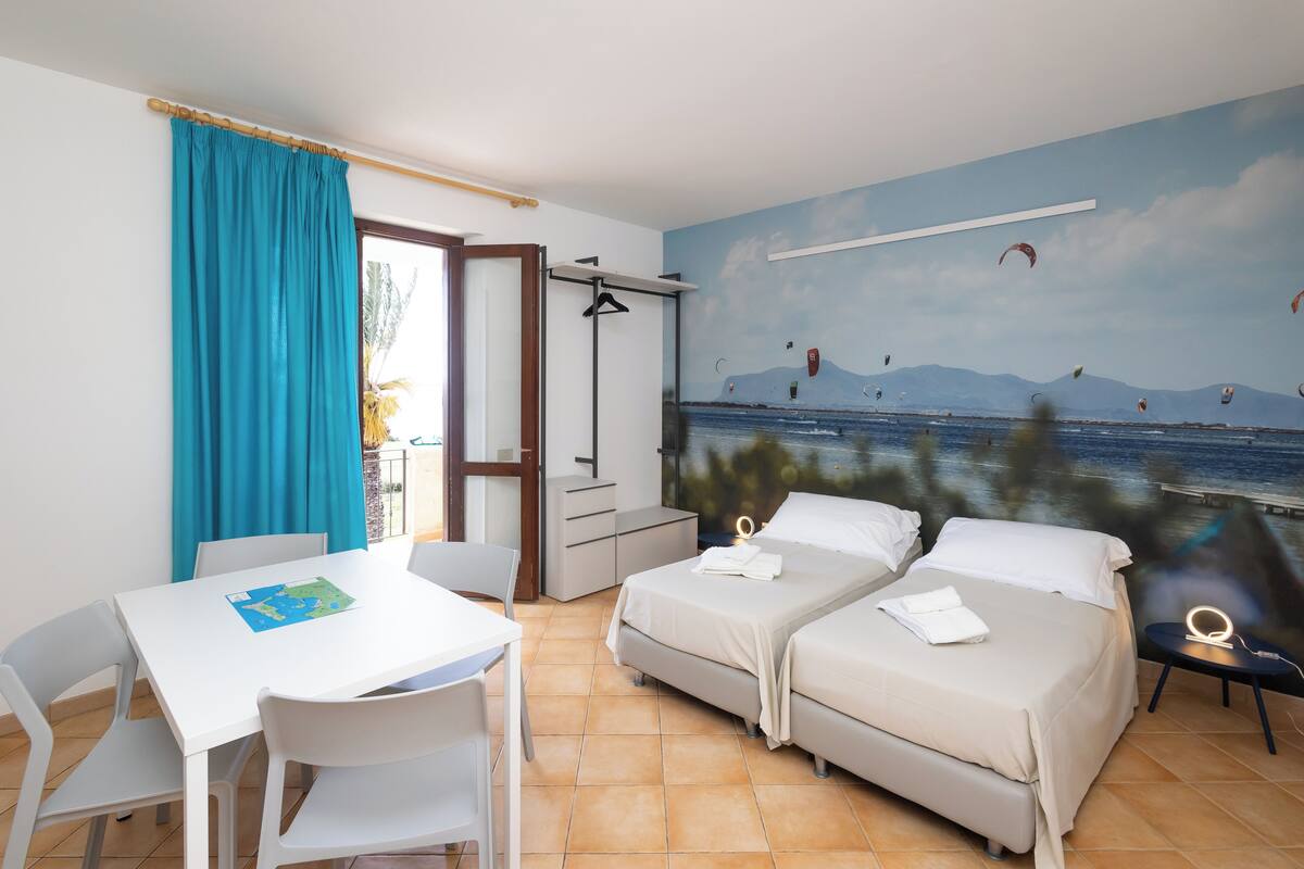 A room with two beds, a table, chairs, a map, and a mural of a beach with kites.