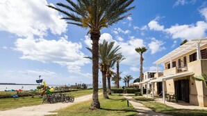 A coastal hotel with palm trees, a beach view, and a pathway leading to the entrance. - Resort Santa Maria (Marsala)