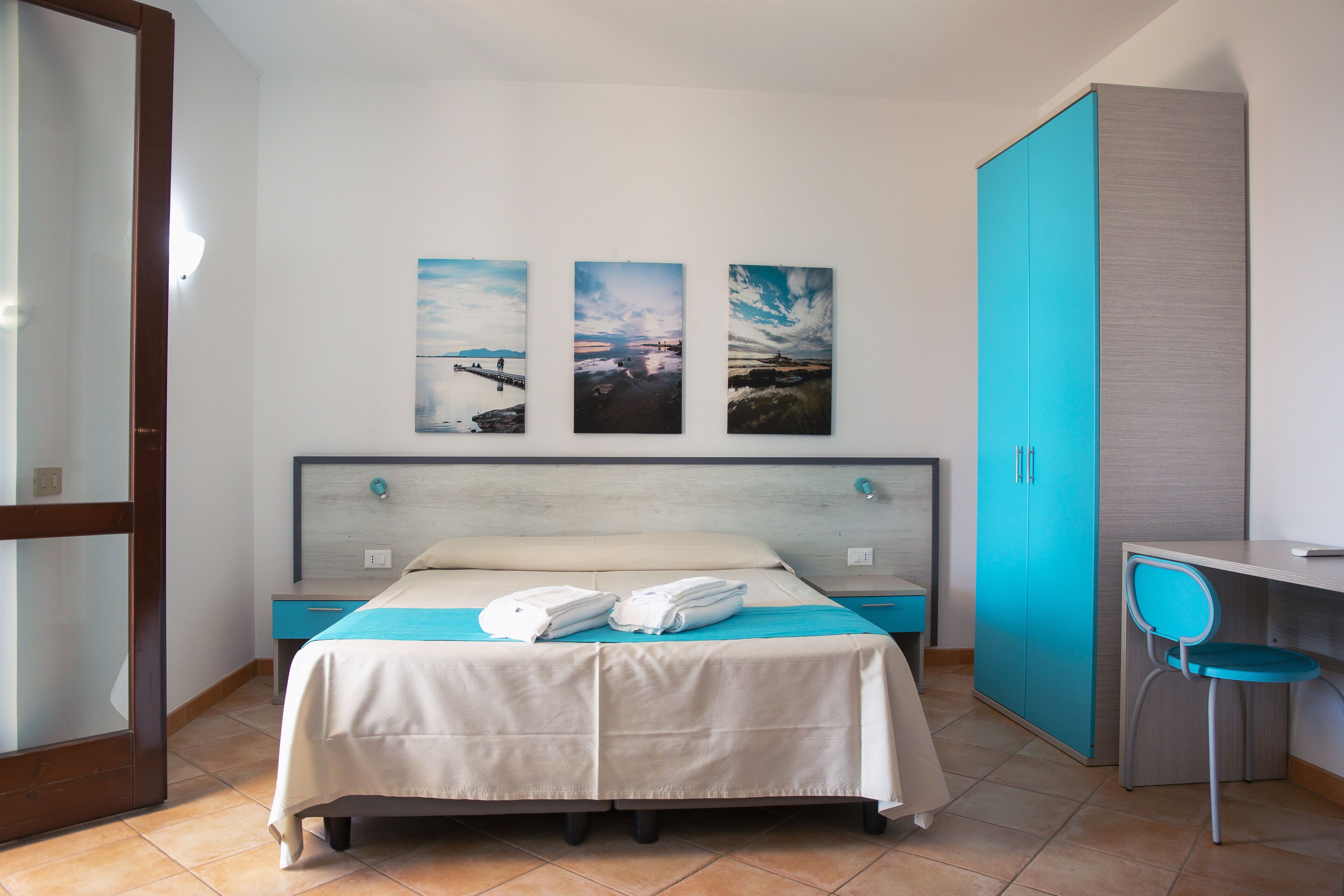 Habitación de hotel con cama, escritorio y silla. Hay tres cuadros en la pared.