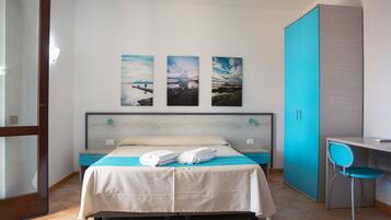 A hotel room with a bed, a desk, and a chair. There are three paintings on the wall.