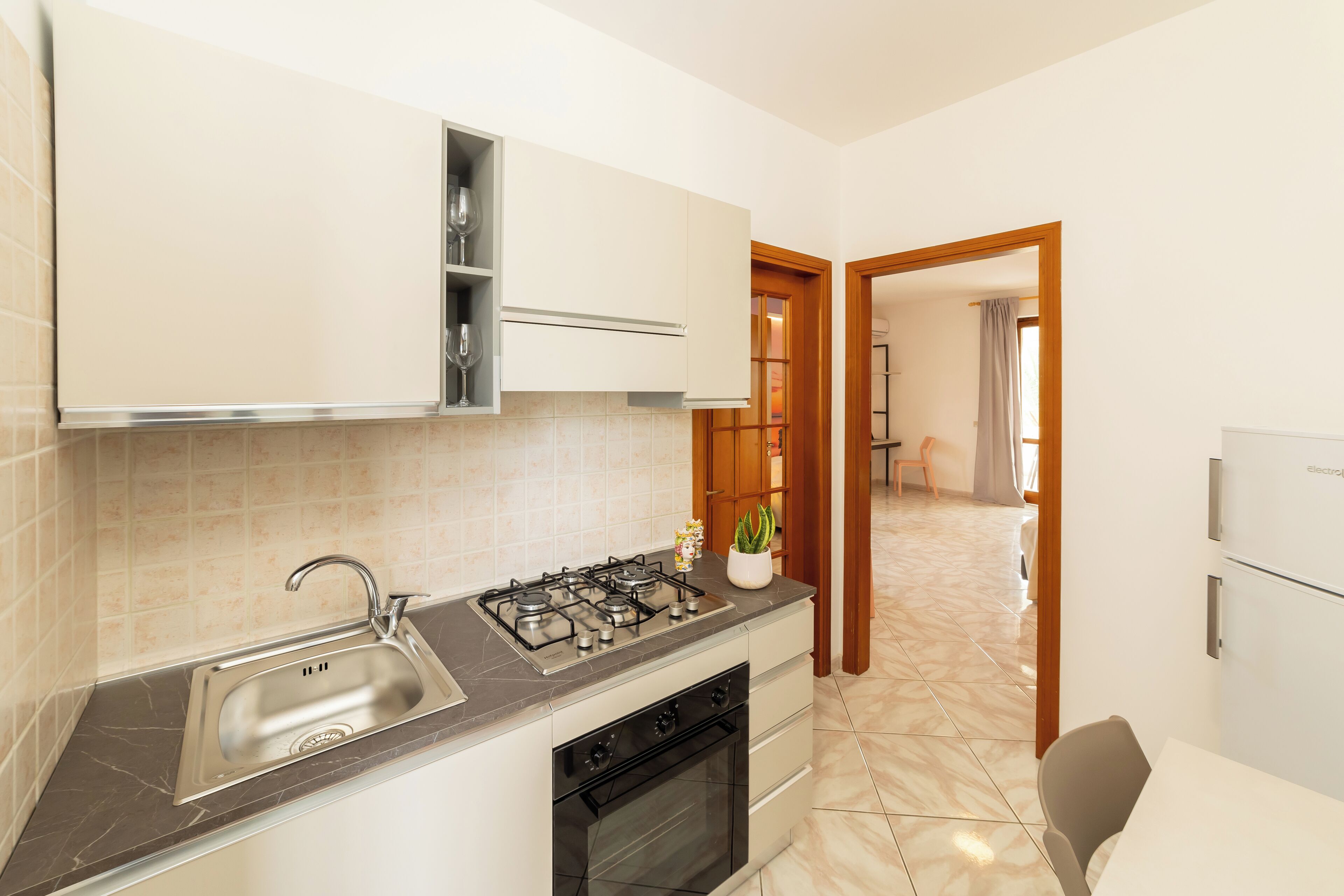 Una cucina compatta con piano cottura a gas, lavello e forno. Sul ripiano c'è una piccola pianta in vaso.