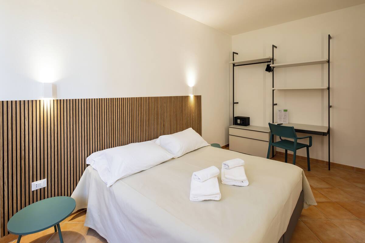 A hotel room with a bed, a desk, a chair, and a small table.