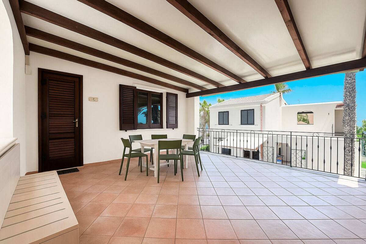 A balcony with a tiled floor, a table with chairs, a wooden door, and a window with shutters.