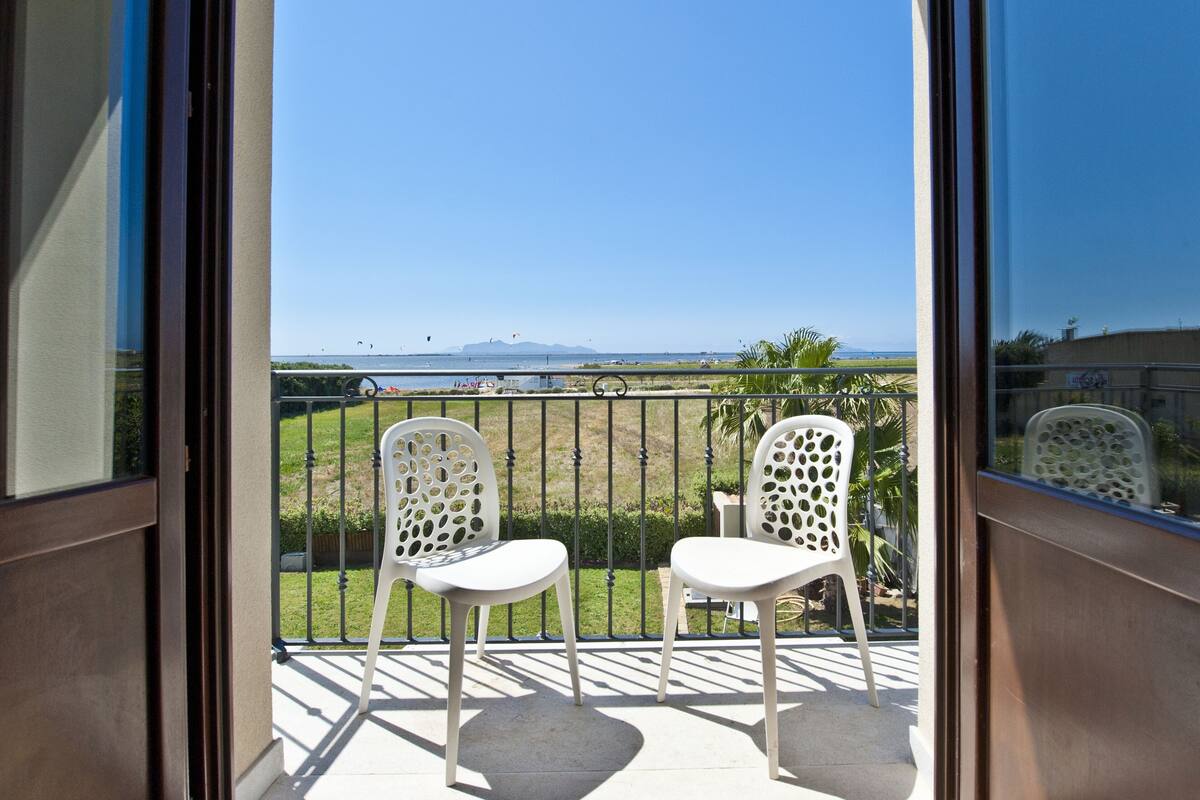 A balcony with two white chairs and a view of a grassy area and water body.