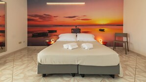 A hotel room with a large bed, two bedside tables, a chair, and a sunset mural on the wall. - Resort Santa Maria (Marsala)