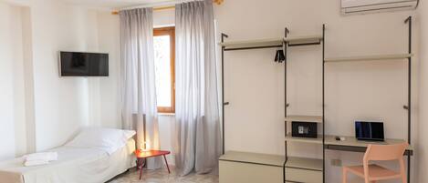 A compact hotel room with a bed, a desk with a laptop, a TV, and a wardrobe.