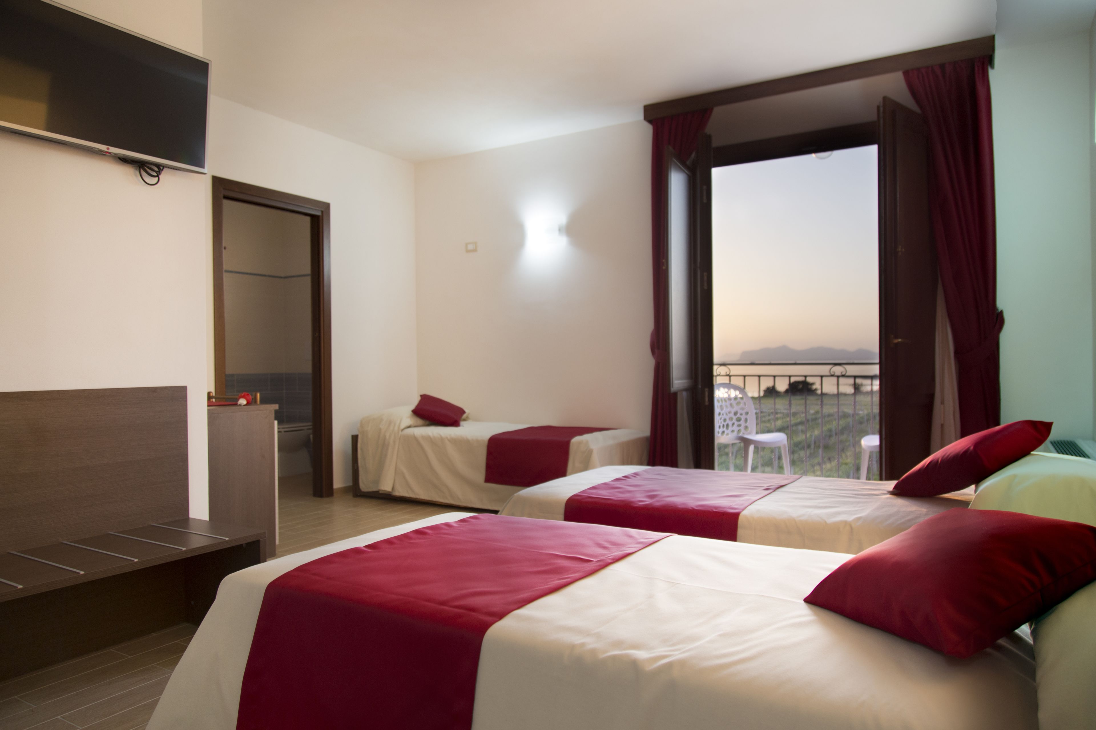 A hotel room with two beds, a TV, a wardrobe, and a balcony with a view.