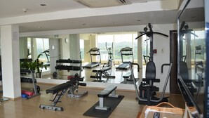 Ein Fitnessraum mit Trainingsgeräten, einer Bank und einem Spiegel, der den Raum widerspiegelt.
